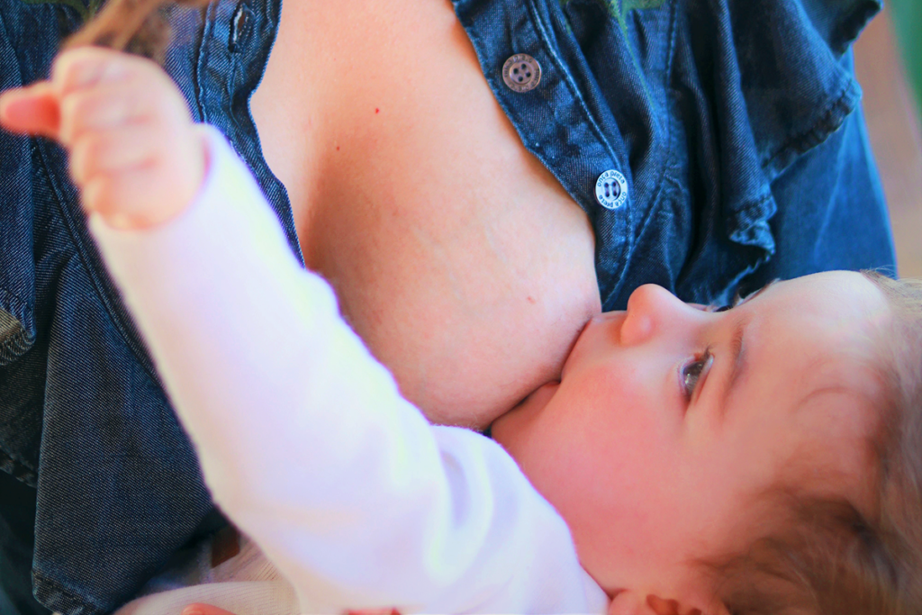 Mamá amamantando a su bebé, mientras este juega con su elo